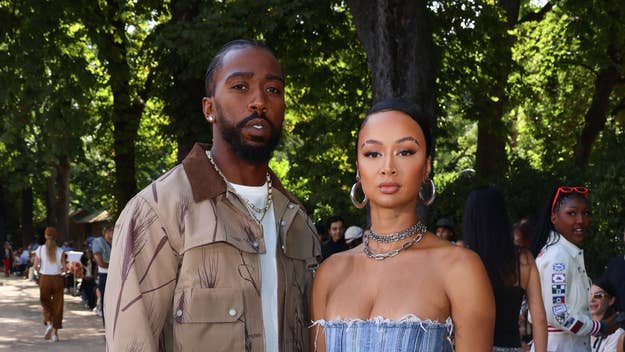 Tyrod Taylor and Draya Michele pose outdoors, with Orlando wearing a jacket and Draya in a strapless dress, surrounded by trees and people in the background