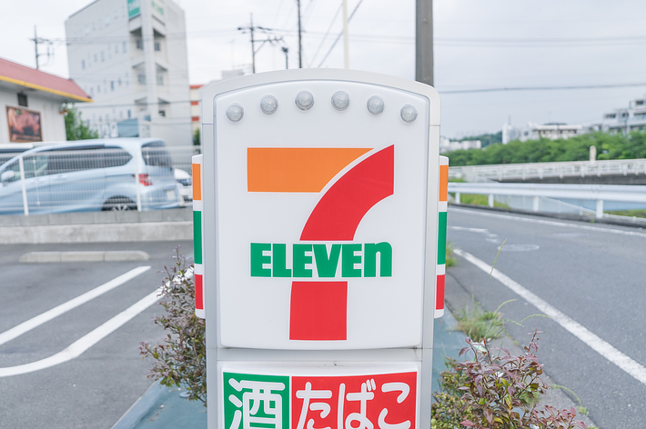 セブンイレブンの看板。下部には、酒、たばこ、銀行ATMと記載されています。