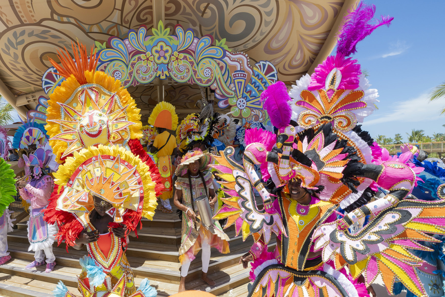 A vibrant carnival scene with people in elaborate, colorful costumes decorated with feathers and intricate patterns, performing on a stage with a festive backdrop