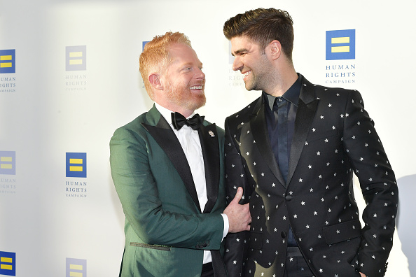 Jesse Tyler Ferguson and Justin Mikita smile and pose together at the Human Rights Campaign event. Jesse wears a green suit, and Justin wears a black suit with star patterns