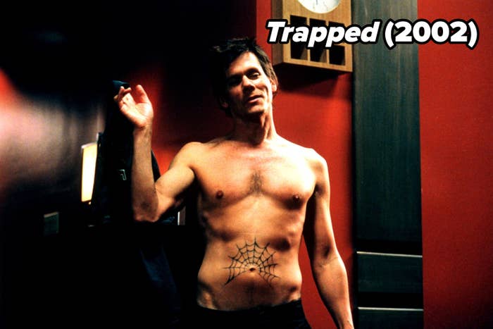 Shirtless man with a spiderweb tattoo on his abdomen stands indoors, raising one hand. A clock and wooden elements are visible in the background