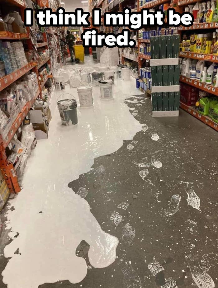 Spilled white paint covers the floor in a store aisle, with paint buckets nearby and footprints tracking through the spill