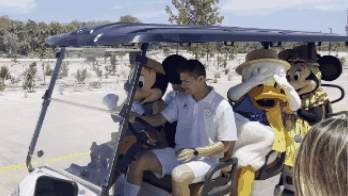 Mickey Mouse, a man in a white outfit, Donald Duck, and Minnie Mouse in a golf cart