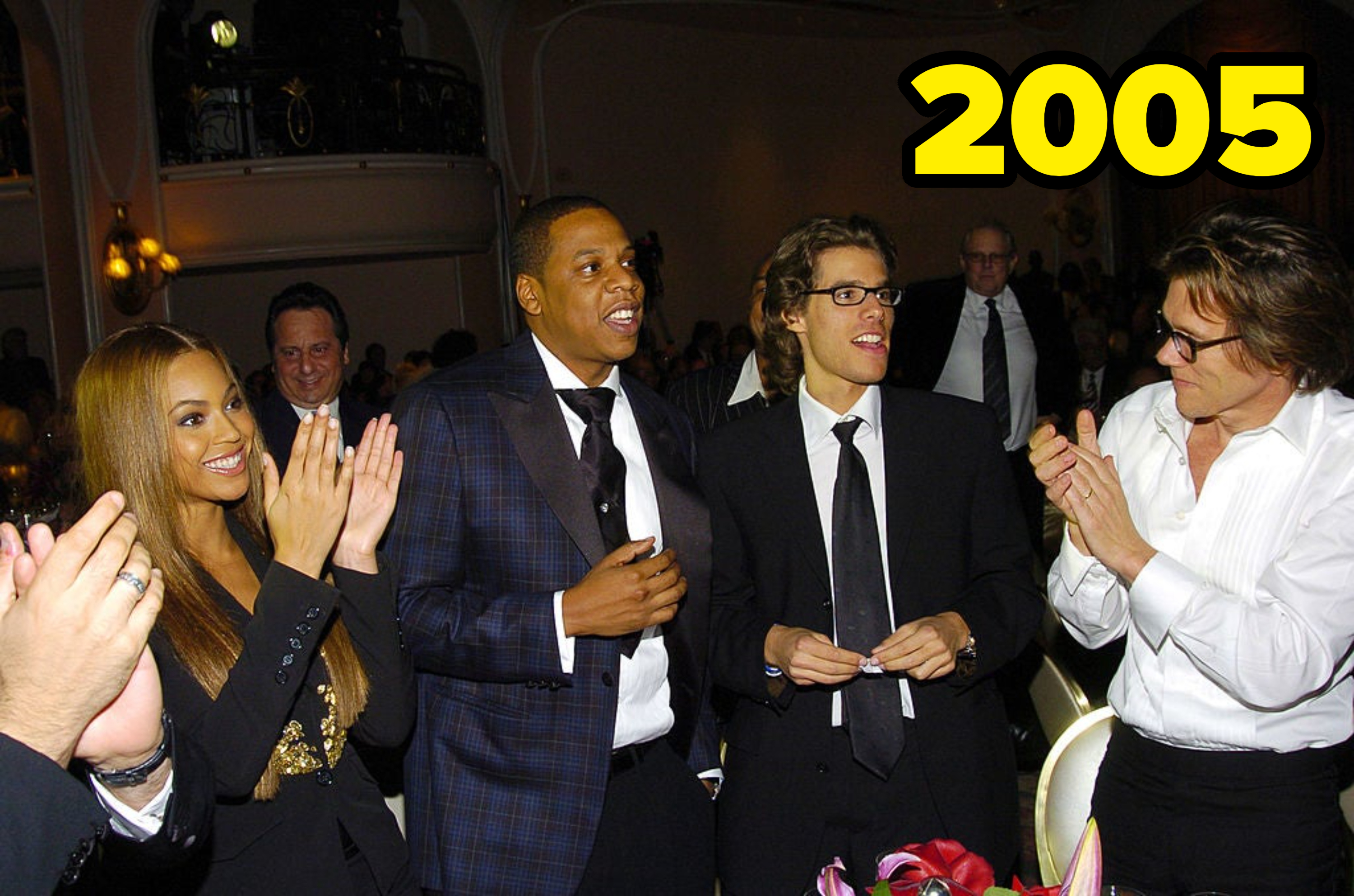 Beyoncé, Jay-Z, and two others dressed in formal wear stand in a fancy venue, smiling and clapping