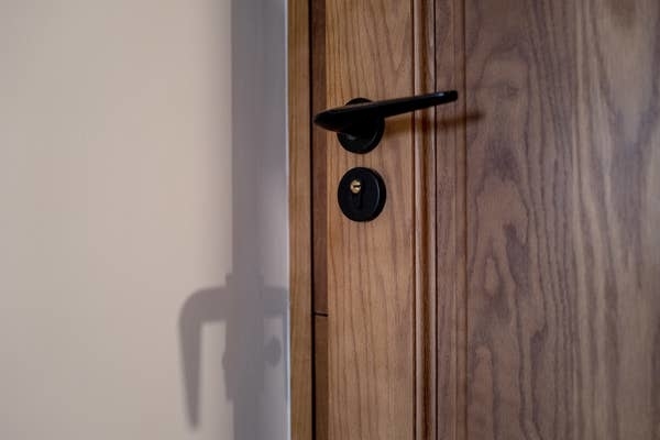 A closed wooden door with a black handle and keyhole, casting a shadow on an adjacent wall