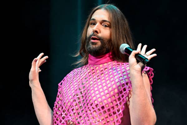 Jonathan Van Ness speaking into a microphone, wearing a mesh top