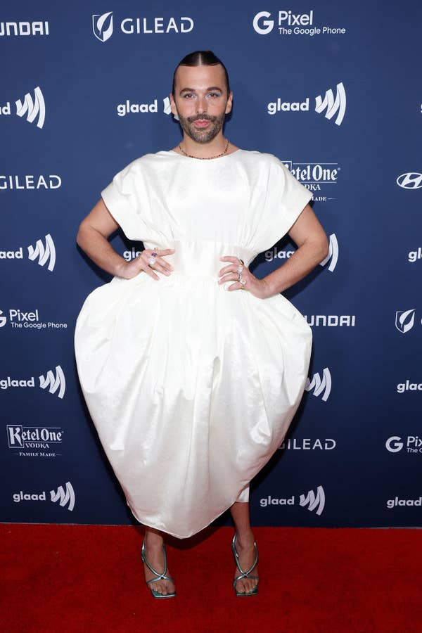 Jonathan Van Ness poses on the red carpet in an extravagant white dress with a voluminous skirt at the GLAAD Media Awards