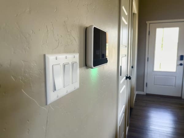 Light switches and a smart thermostat mounted on a wall in a hallway with a door at the end