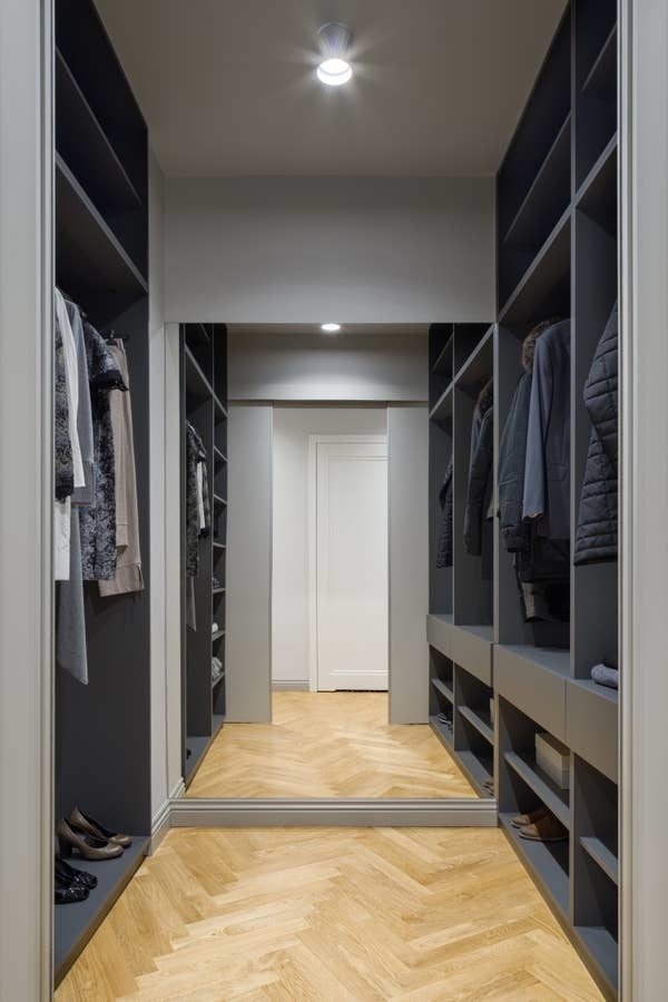 A modern, well-organized walk-in closet with clothes hanging on both sides and shelves at the bottom for shoes. Cloakroom features a large mirror at the end