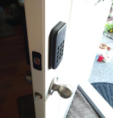 Smart lock installed on a door, shown from the inside, with a door handle and part of a house interior visible in the background