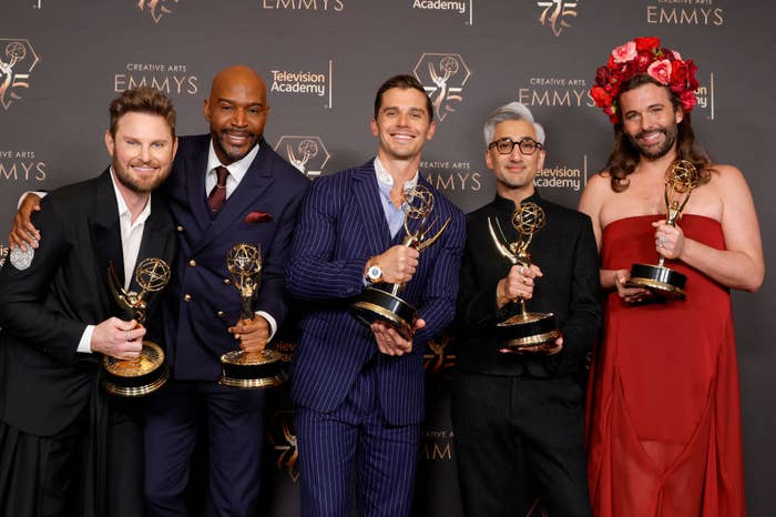 Karamo Brown, Tan France, Bobby Berk, Antoni Porowski, and Jonathan Van Ness holding Emmy awards at the Creative Arts Emmys. Jonathan wears a red dress with a flower crown