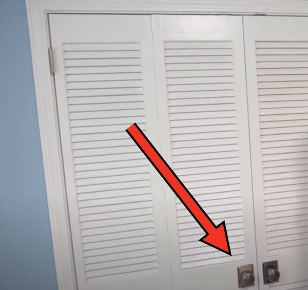 Two white louvered closet doors with a large red arrow pointing downward toward the door handles
