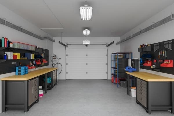 Organized garage with workbenches, tools on shelves, storage cabinets, and a closed garage door in the background