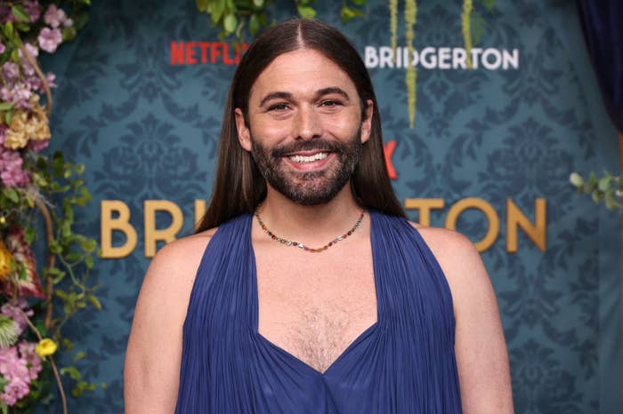 Jonathan Van Ness, wearing a sleeveless, flowing dress, smiles at the "Bridgerton" Netflix event