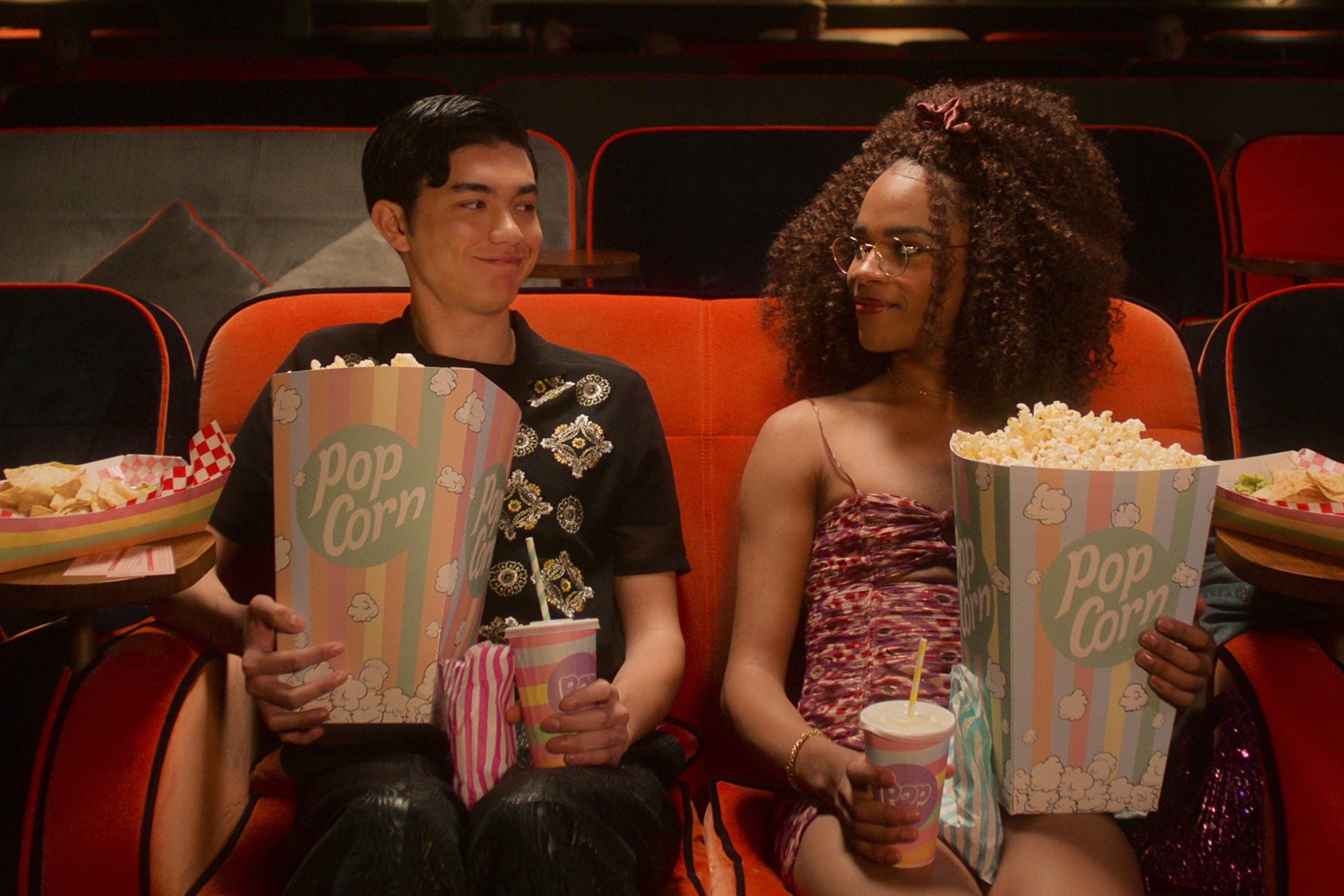 Will Gao and Yasmin Finney sit in a movie theater holding popcorn and drinks, smiling at each other
