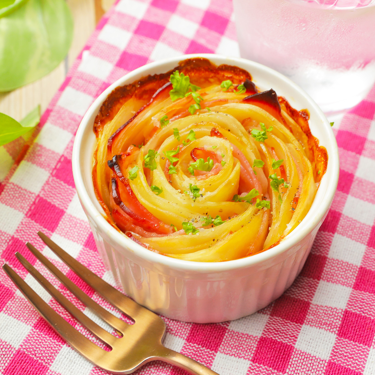 テーブルの上に置かれた白い陶器のラメキンに、薔薇の形に盛り付けられたポテトがある。隣にはフォークが置かれている。