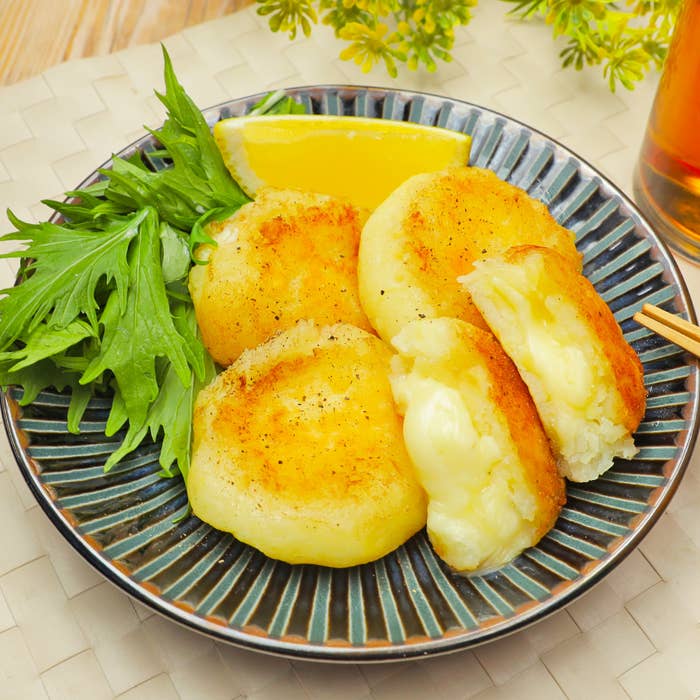 お皿に盛られたジャガイモのチーズフライ、レモンのくし切りとサラダ野菜が添えられています。