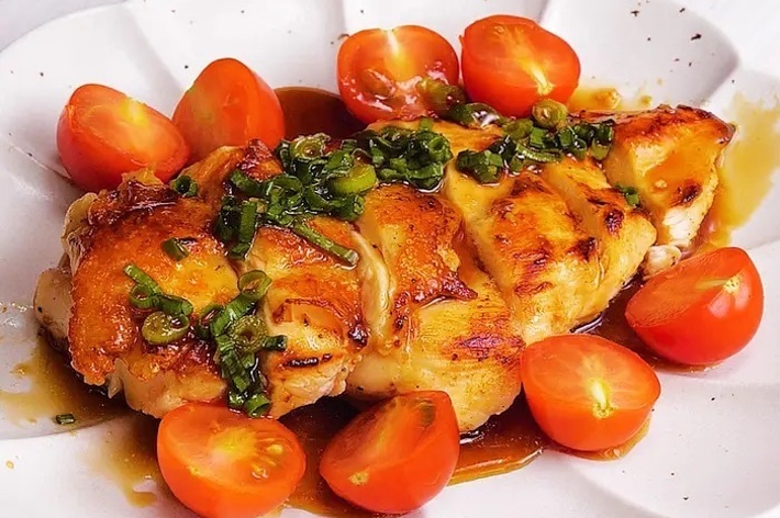 お皿に盛り付けられた鶏肉料理とミニトマトの画像。