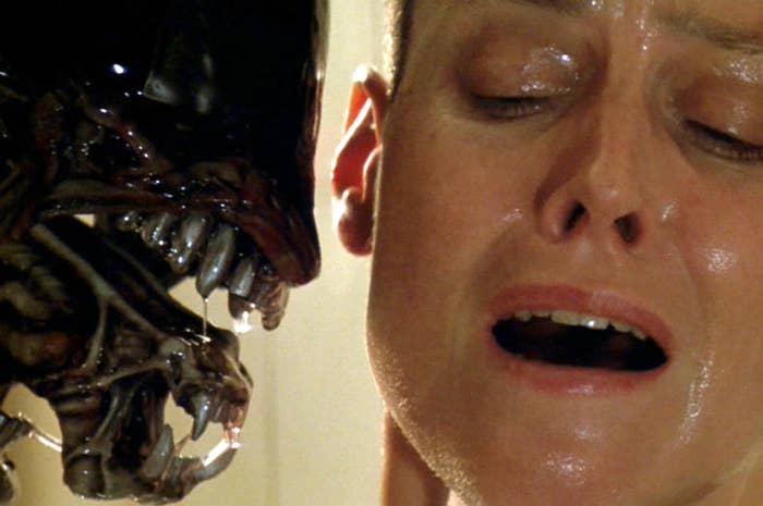 Sigourney Weaver in close-up with an alien creature from the film "Alien." The alien bares its teeth near her face as she appears to be in distress