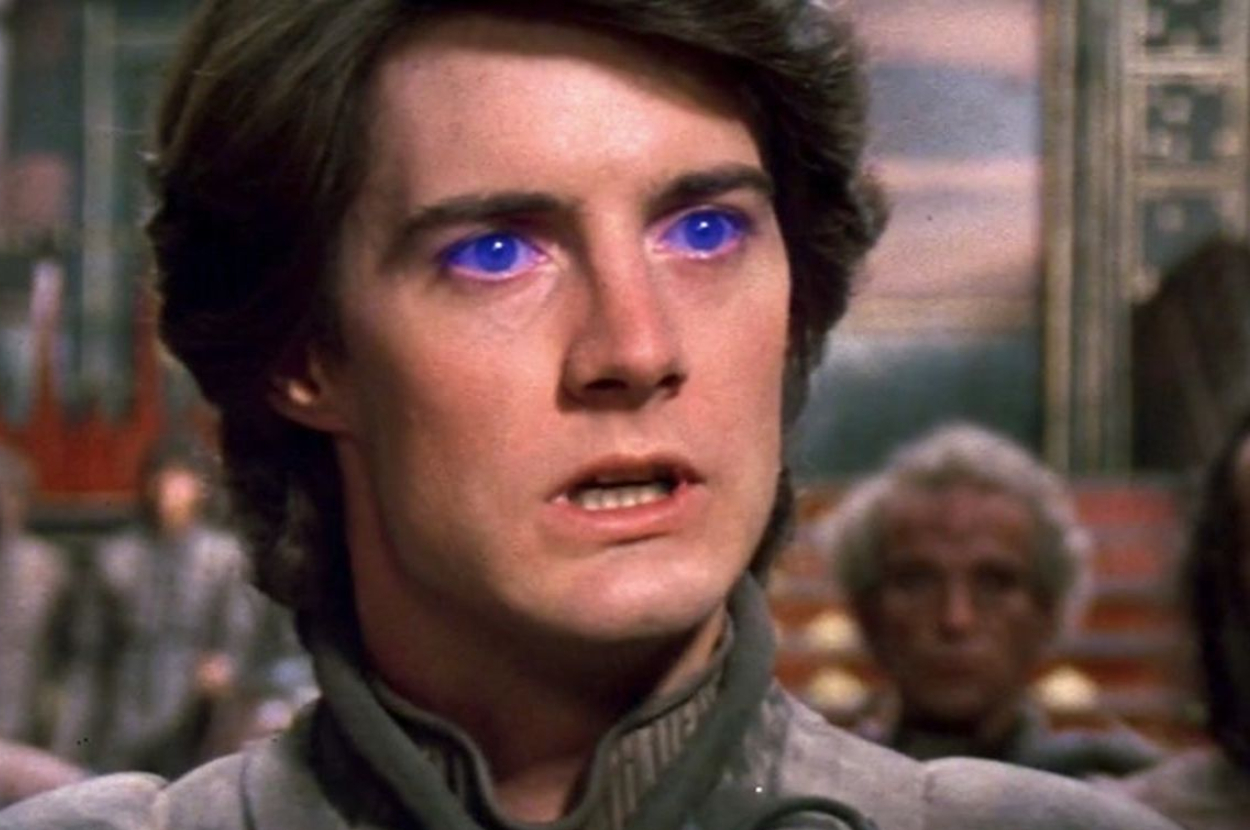 Kyle MacLachlan, portraying Paul Atreides from Dune, stares ahead with glowing blue eyes, indicating spice addiction
