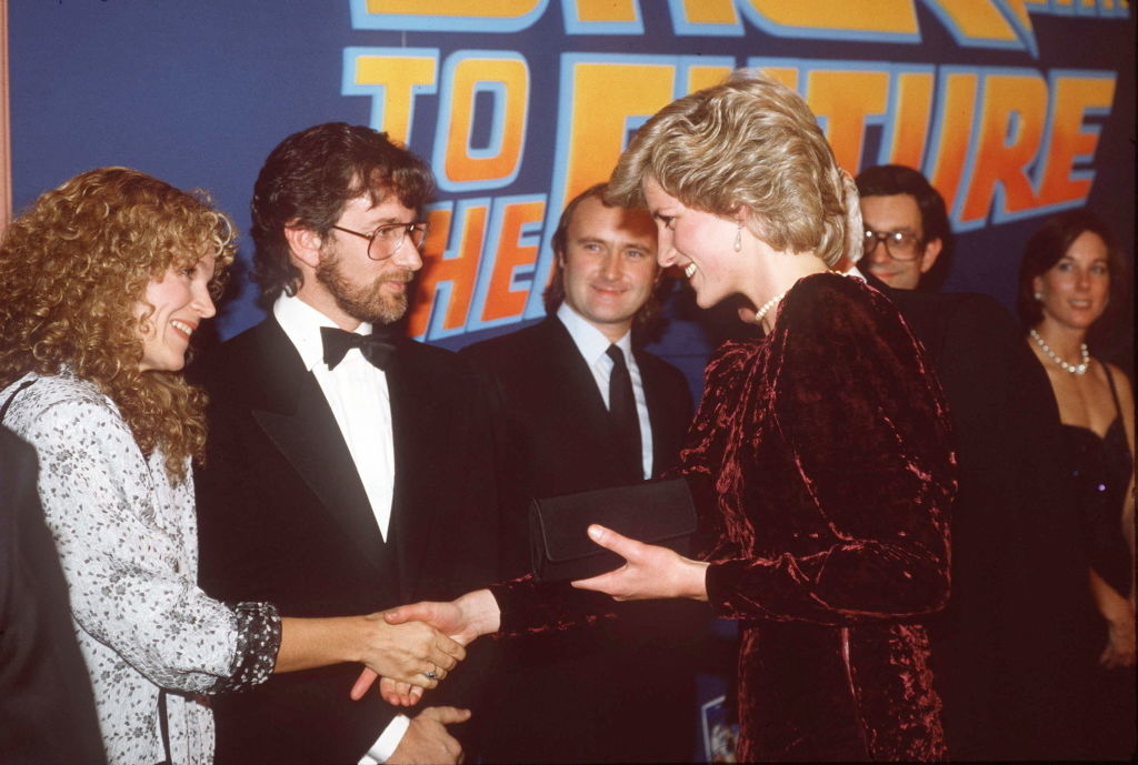 Sarah Jessica Parker shakes hands with Princess Diana at "Back to the Future" event, with Steven Spielberg, Phil Collins, and others in the background