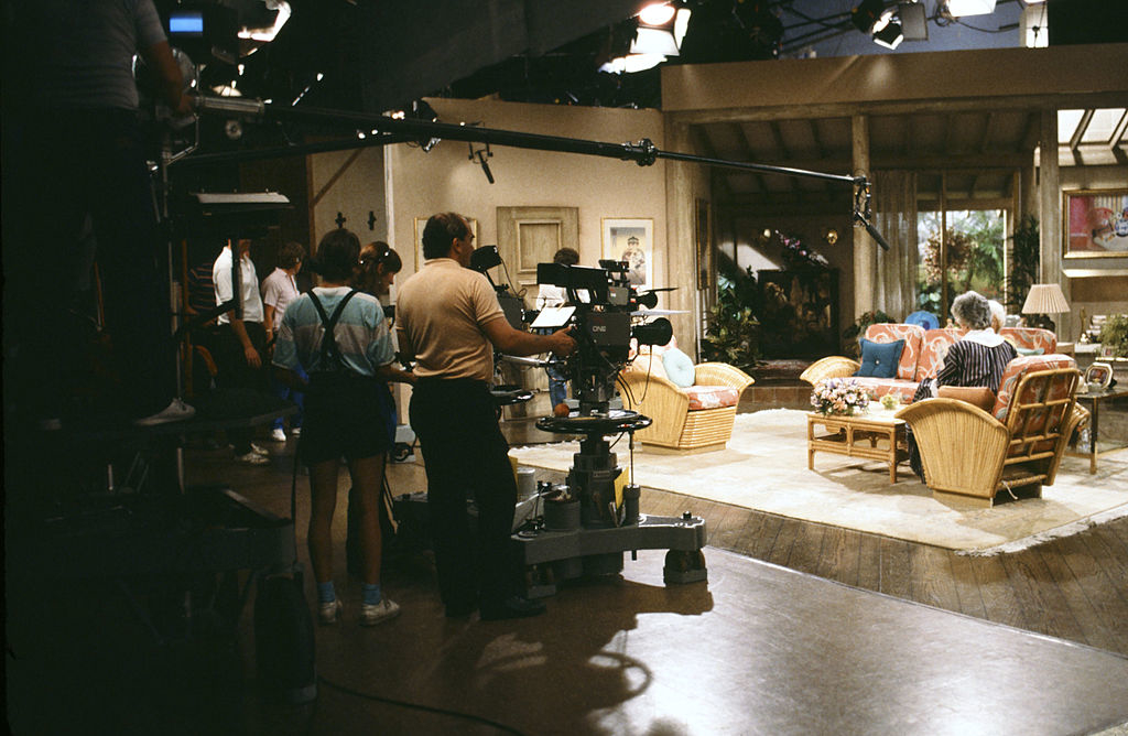 Filming crew on the set of "The Golden Girls" with actors rehearsing a scene in the living room set. Camera and boom operators are preparing for a shoot
