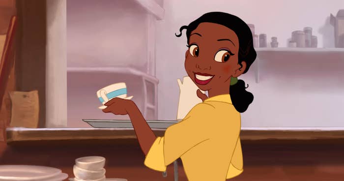 Tiana from The Princess and the Frog holds a cup while smiling in a kitchen