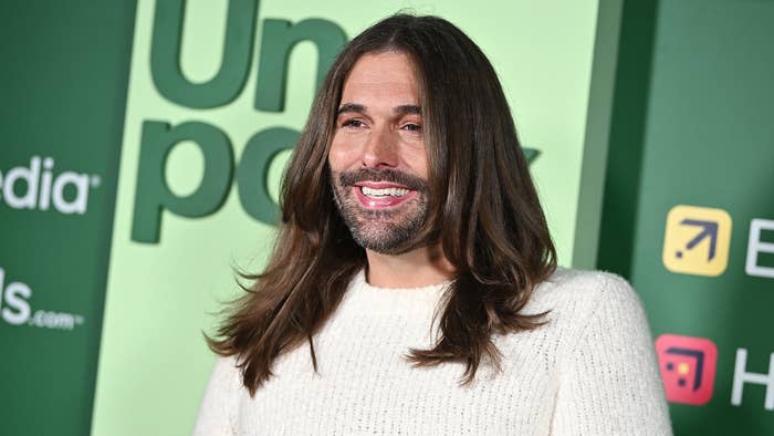 Jonathan Van Ness smiles at a media event, wearing a white sweater