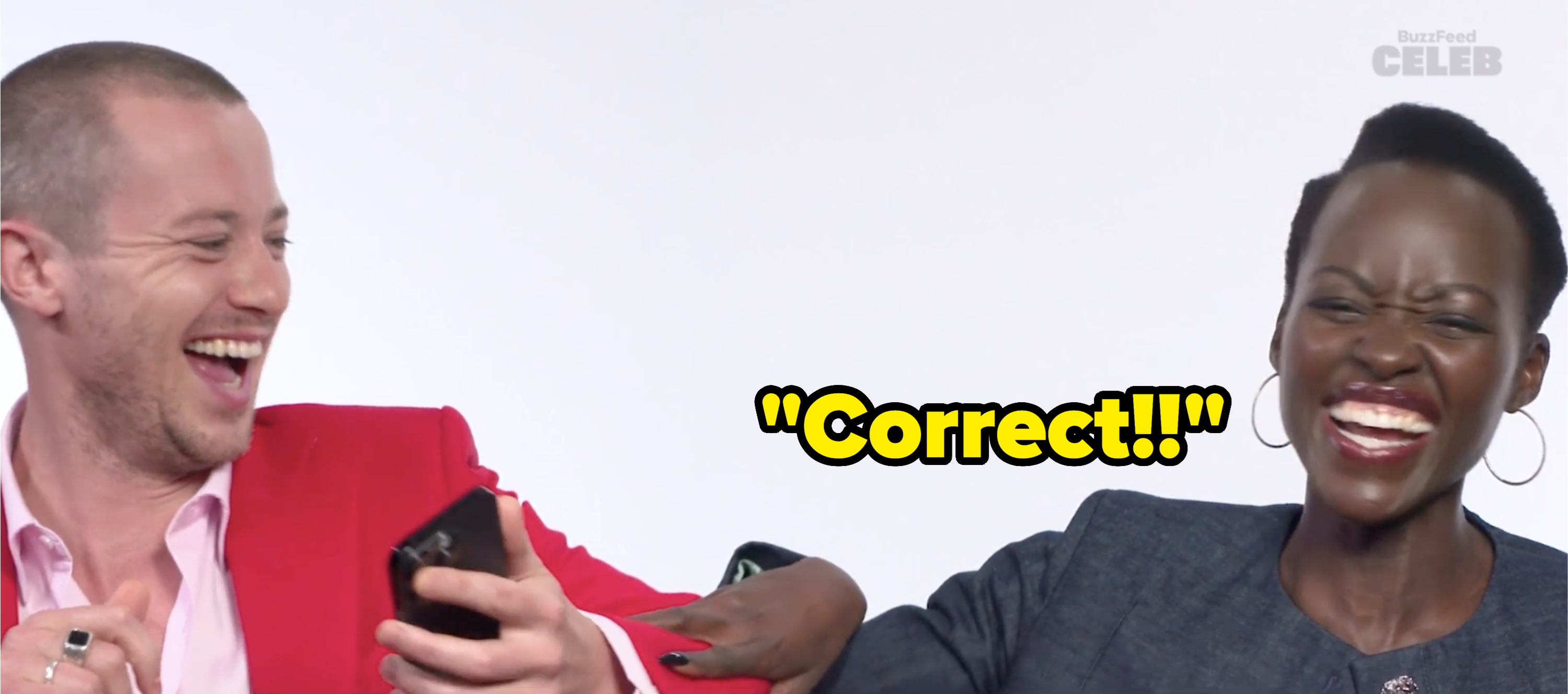 Joseph Quinn and Lupita Nyong'o laughing together while holding smartphones, during a BuzzFeed Celeb interview