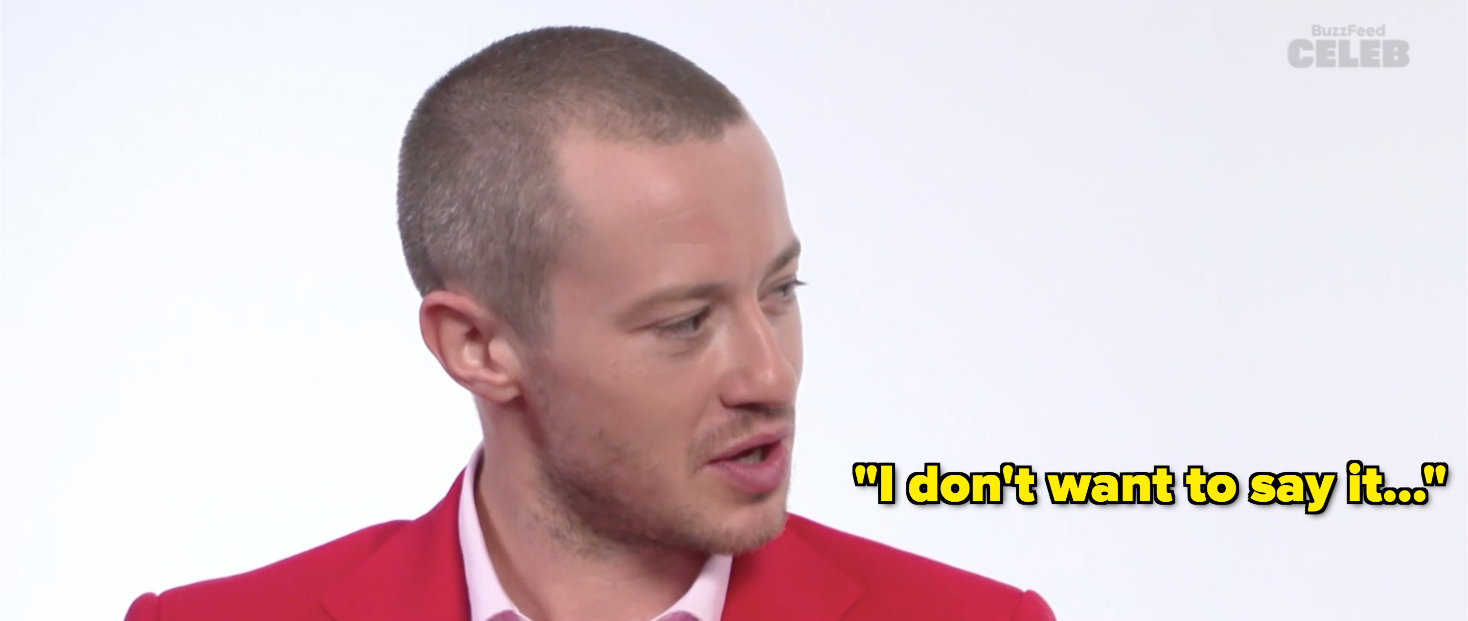 A person dressed in a sharp outfit is engaging in conversation. The image has a BuzzFeed Celeb watermark in the top right corner