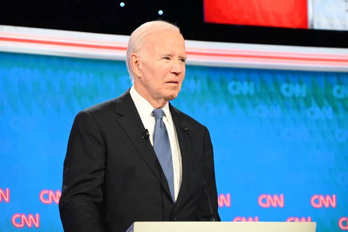 Joe Biden speaking at a CNN event, standing at a podium, wearing a dark suit, white shirt, and blue tie