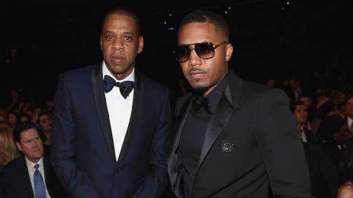 Jay-Z and Nas at a music event, both dressed in formal black suits, with Nas wearing sunglasses