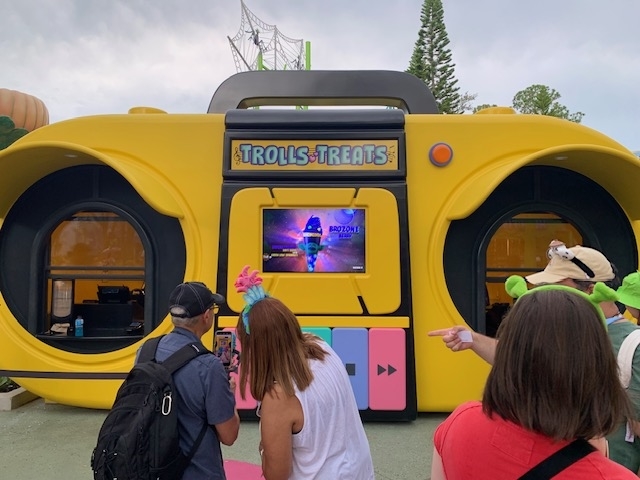 People gather around a large, colorful Trolls-treats themed booth shaped like a boombox, with a screen displaying Poppy from the movie Trolls World Tour