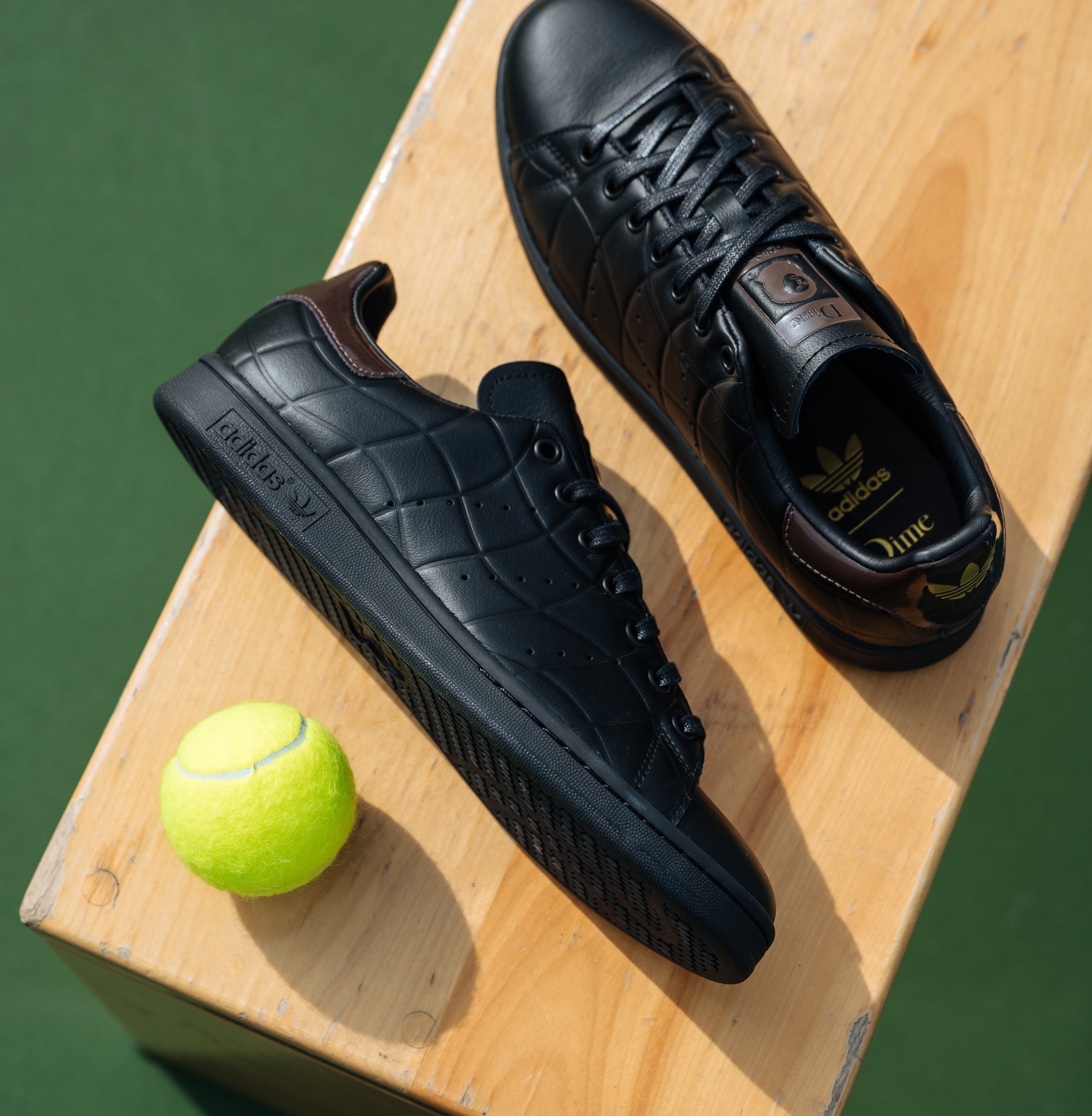 Pair of black Adidas sneakers on a wooden box with a tennis ball nearby