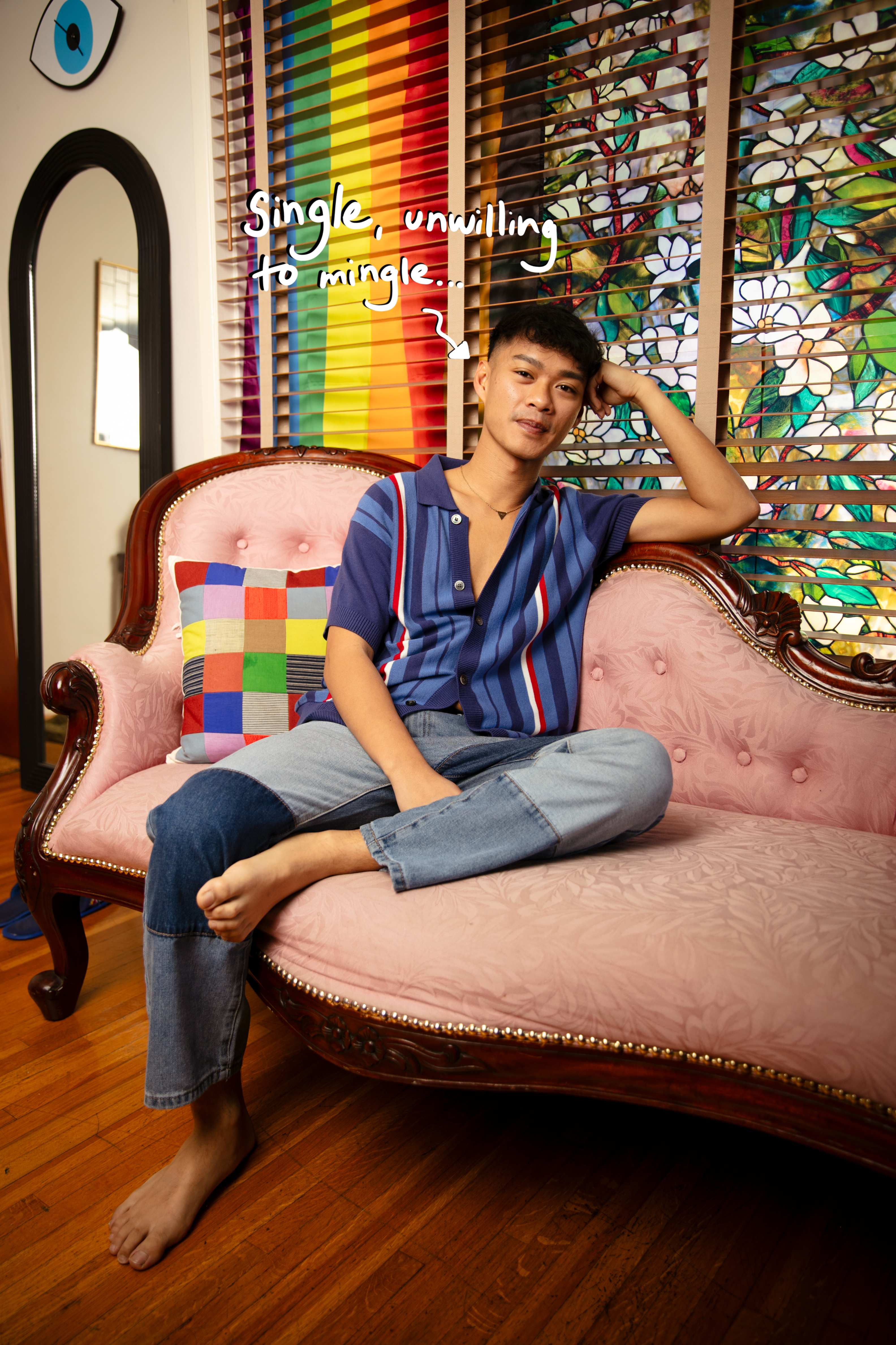 A person sits on a patterned couch with a rainbow flag in the background, wearing a striped shirt. Handwritten text reads, "Single, unwilling to mingle&hellip;"