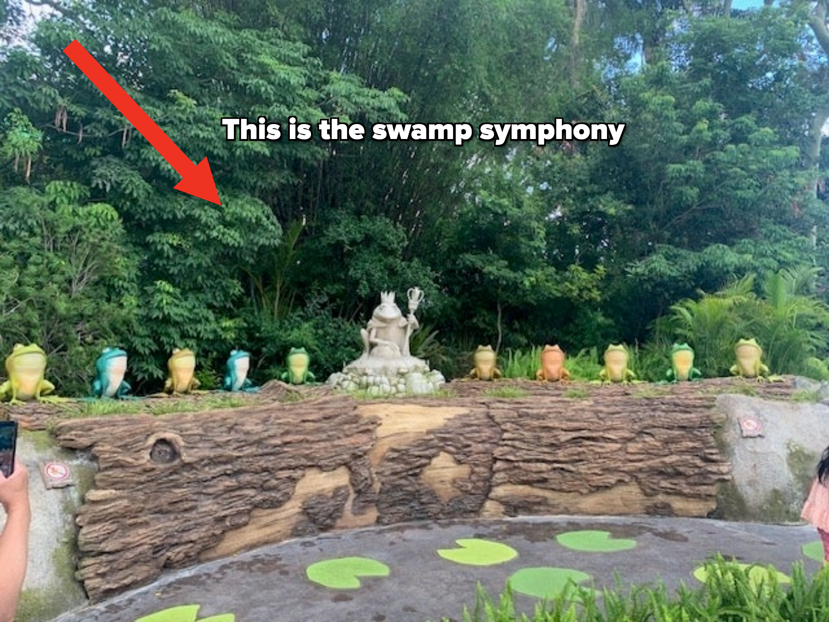 Statues of Kermit and Miss Piggy are surrounded by colorful Kermit sculptures in a garden setting