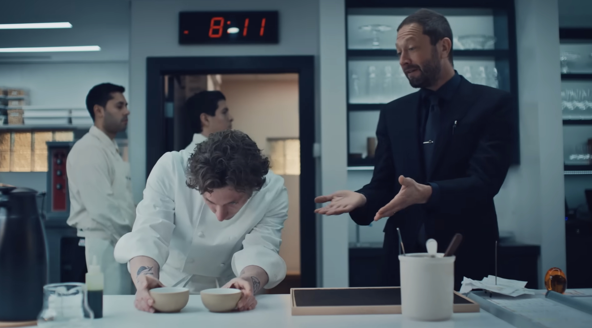 Jeremy Allen White looking at bowls in a kitchen and Ebon Moss-Bachrach speaking to him with his hands extended in the "The Bear"