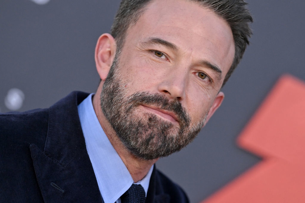 Ben Affleck, wearing a suit jacket and shirt, poses against a patterned background