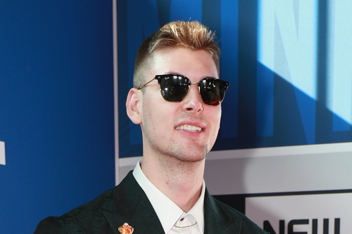 Man wearing sunglasses and a formal jacket with a lapel pin at an event