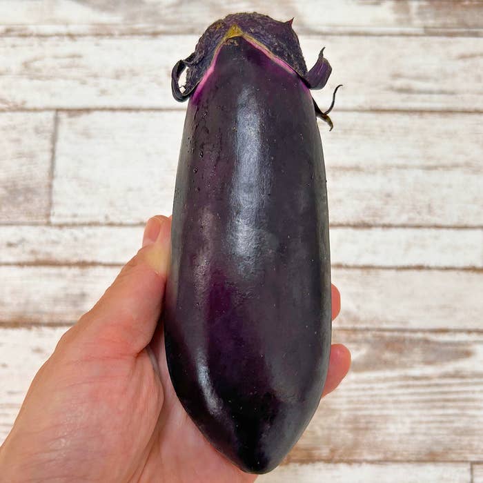 手に持たれたなすの写真。背景は木目のテーブル。