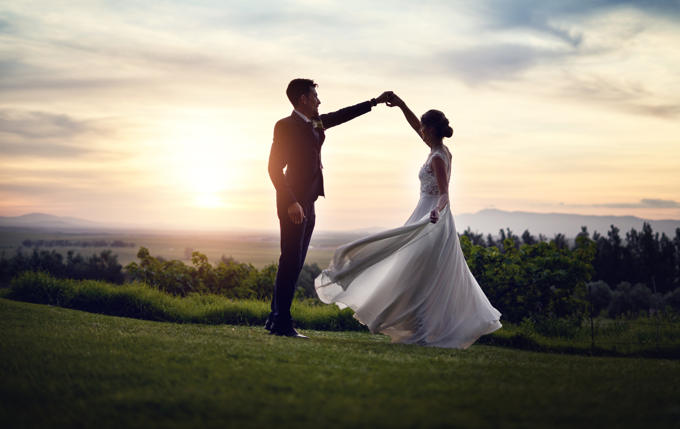 A couple dances outside at sunset, with the woman in a flowing dress and the man in a suit