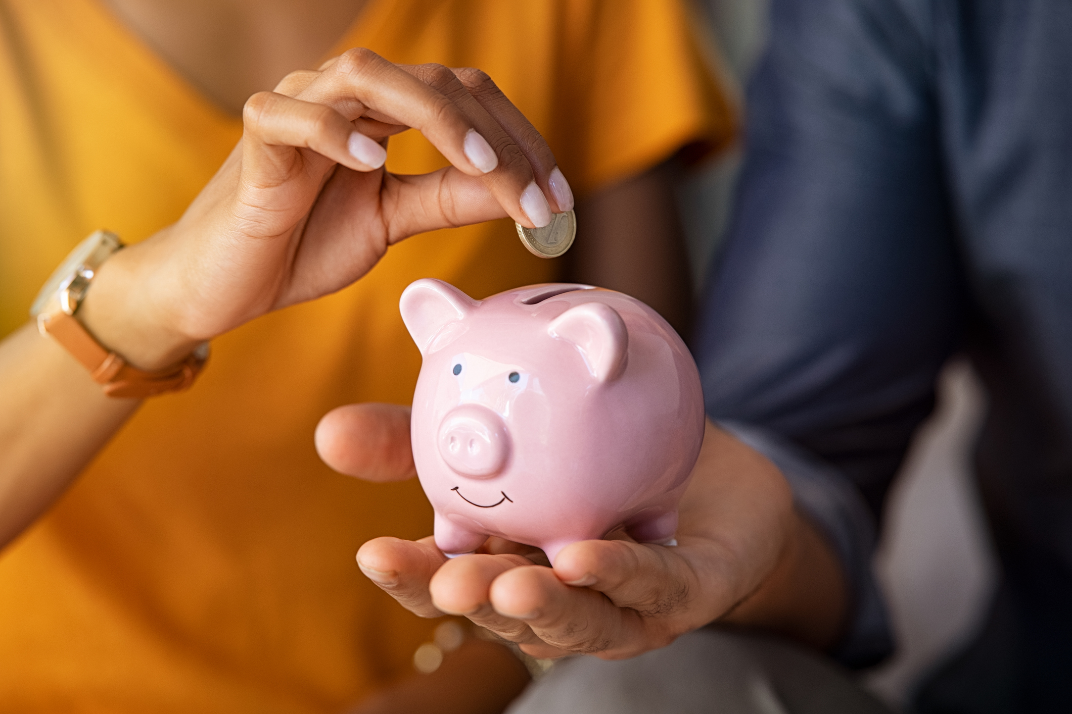 Two people depositing a coin into a piggy bank, illustrating savings and financial planning