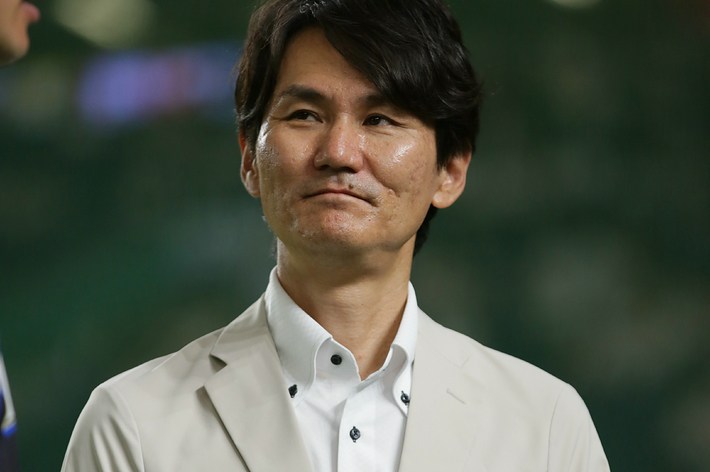 知らない人がベージュのジャケットを着てカメラの方向に微笑んでいる。