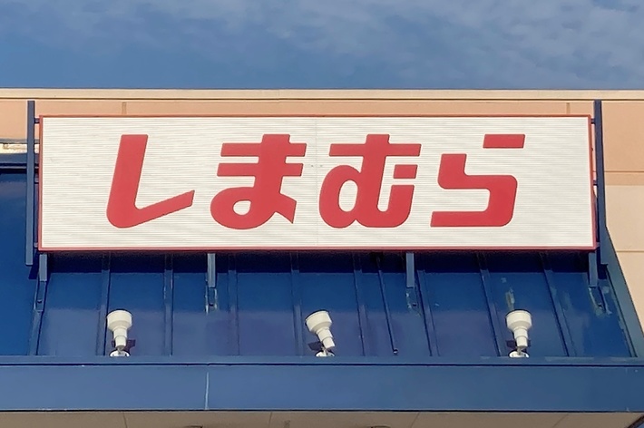 The image shows a store with a sign in Japanese that reads &ldquo;しまむら&rdquo;. There is a handicap parking sign visible in the foreground