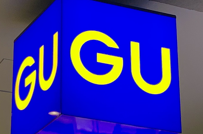 Illuminated cube sign with yellow &ldquo;GU&rdquo; letters on a blue background, hanging from the ceiling