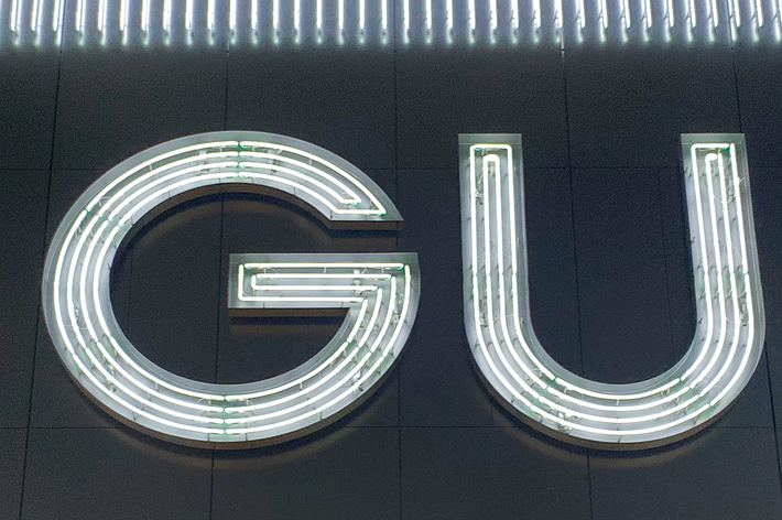 Illuminated GU sign on a building facade at night, featuring continuous neon lighting accents