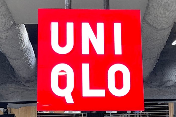 UNIQLO store sign hanging from the ceiling, with shelves of neatly stacked clothing below