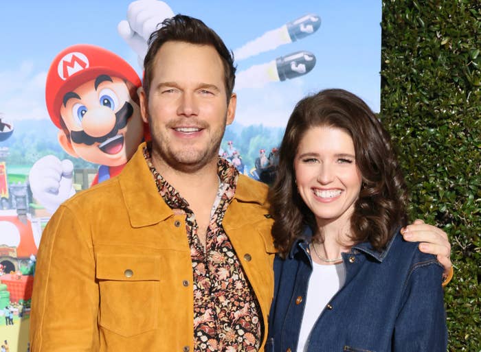 Chris Pratt, in a casual jacket, and Katherine Schwarzenegger, in a denim jacket, smile at a movie premiere with a Mario theme in the background