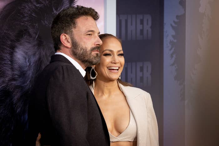 Ben Affleck and Jennifer Lopez pose together on the red carpet. Ben wears a suit, and Jennifer wears a stylish two-piece outfit with a blazer