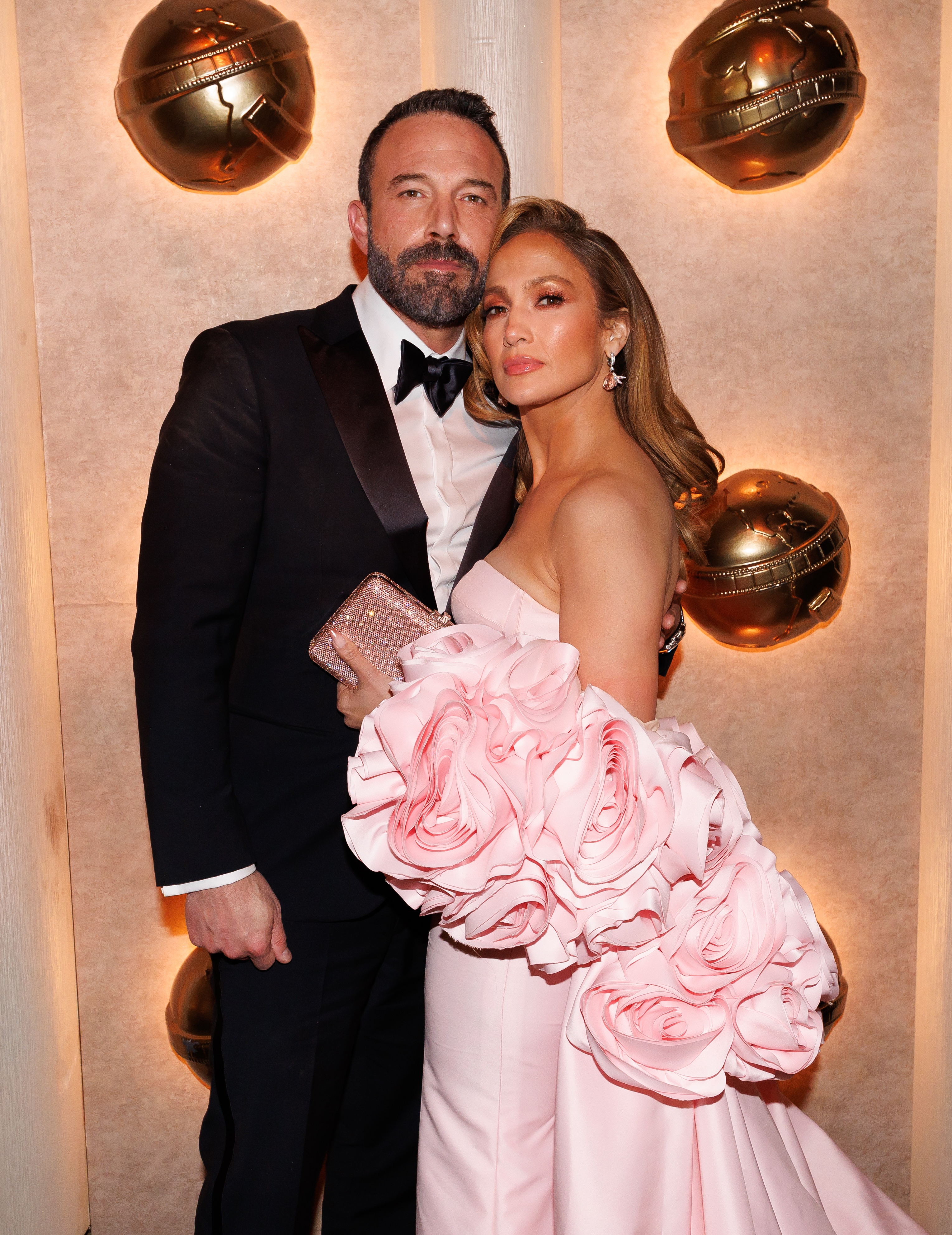 Ben Affleck and Jennifer Lopez on the red carpet; Ben wears a tuxedo while Jennifer wears a strapless gown with large floral accents